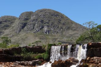 Cachoeira desliza por um paredão rochoso na Serra do Cipó, em meio à vegetação natural.