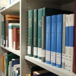 Estantes organizadas com livros em uma biblioteca contemporânea, representando acervo, preservação e acesso ao conhecimento.
