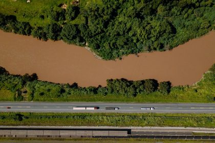 Vista aérea de caminhões trafegando por uma estrada às margens de um rio em Coronel Fabriciano, Minas Gerais