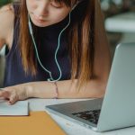 Estudante faz anotações enquanto utiliza um laptop para acompanhar atividades acadêmicas.