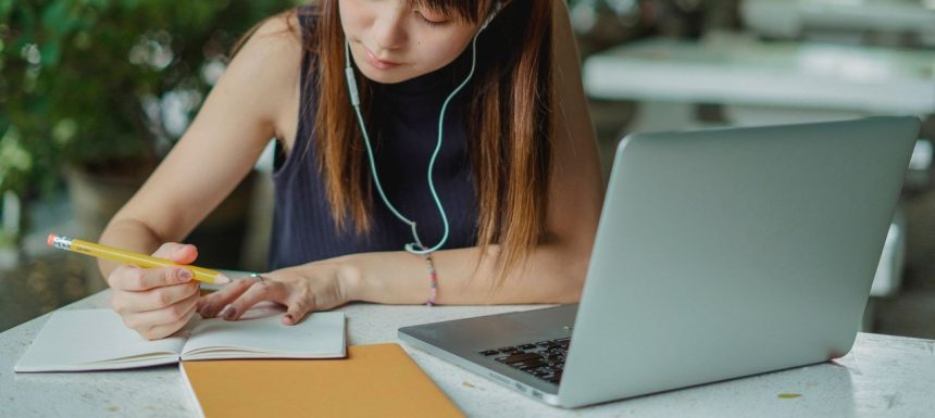 Estudante faz anotações enquanto utiliza um laptop para acompanhar atividades acadêmicas.